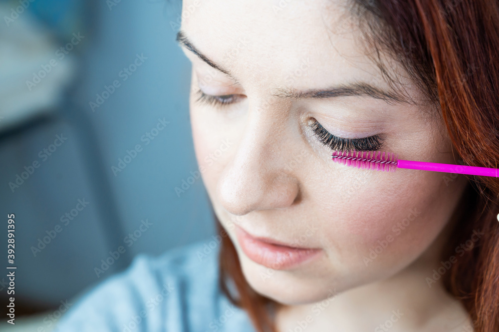 Red head woman brushing her extension eyelashes with a brush. girl with impending eyelid make-up mascara. Beauty industry. Red head woman brushing her extension eyelashes with a brush. girl with impending eyelid make-up mascara. Beauty industry.