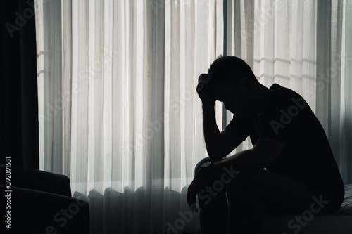 Silhouette depressed man sadly sitting on the bed in the bedroom, depression concept photo