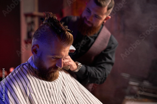 confident male hairstylist cut hair to elegant stylish man sitting in salon, young male enjoy the process of cutting
