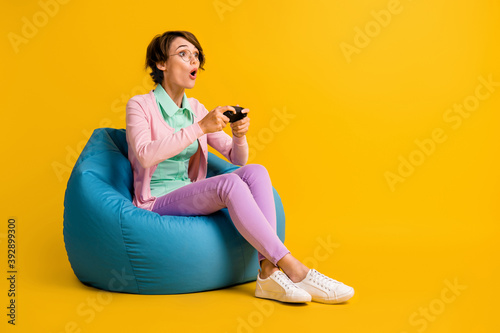 Full length body size photo of girl playing console with controller amazed in glasses isolated on bright yellow color background copyspace