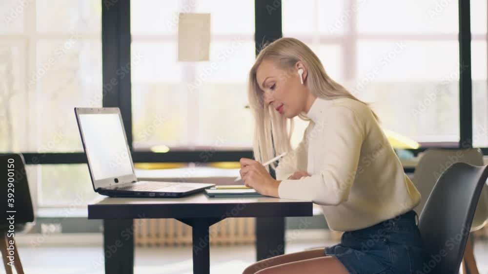 Beautiful young female sitting at table, using tablet and enjoying song in headphone. Caucasian woman listening to music on phone and dancing in workplace. Technology, app, online concept. Beautiful young female sitting at table, using tablet and enjoying song in headphone. Caucasian woman listening to music on phone and dancing in workplace. Technology, app, online concept.