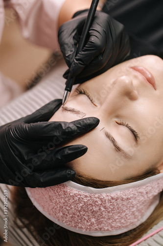 Close-up girl s face with closed eyes. The hand of a master beautician draws a sketch of an eyebrow with a black pen on the girl s skin before microblading