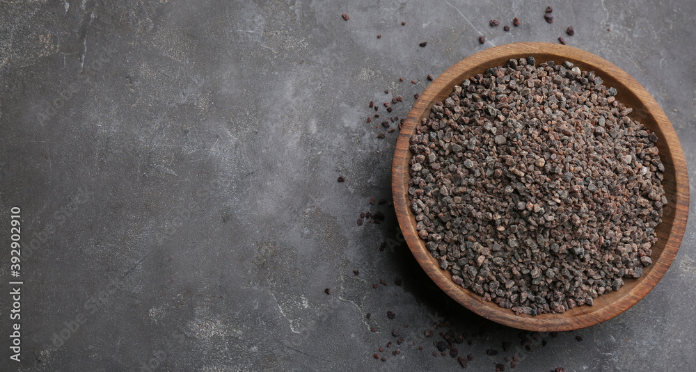 Black salt in wooden bowl on grey table, top view. Space for text Black salt in wooden bowl on grey table, top view. Space for text