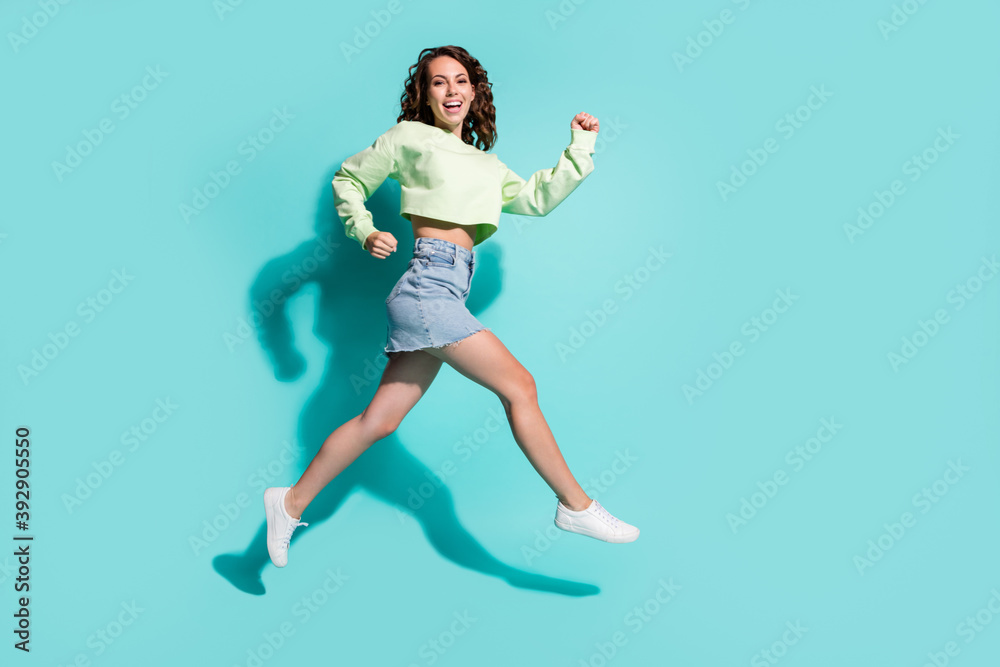 Full length body size side profile photo of girl jumping high hurrying up laughing smiling isolated on vivid teal color background