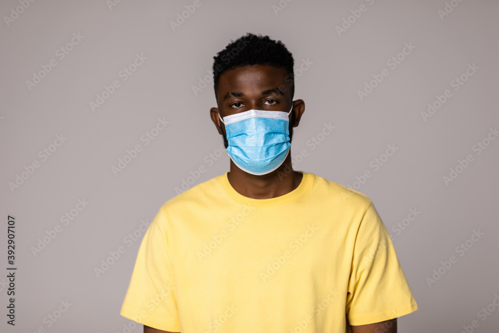 Health, pandemic and safety concept. Young african american young man wearing face protective medical mask for protection from virus disease over grey background Health, pandemic and safety concept. Young african american young man wearing face protective medical mask for protection from virus disease over grey background