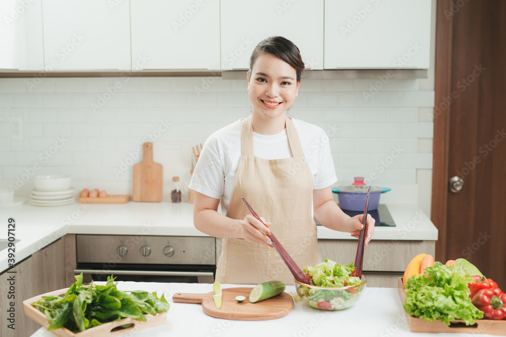 Smiling young woman in apron stand in modern kitchen preparing salad