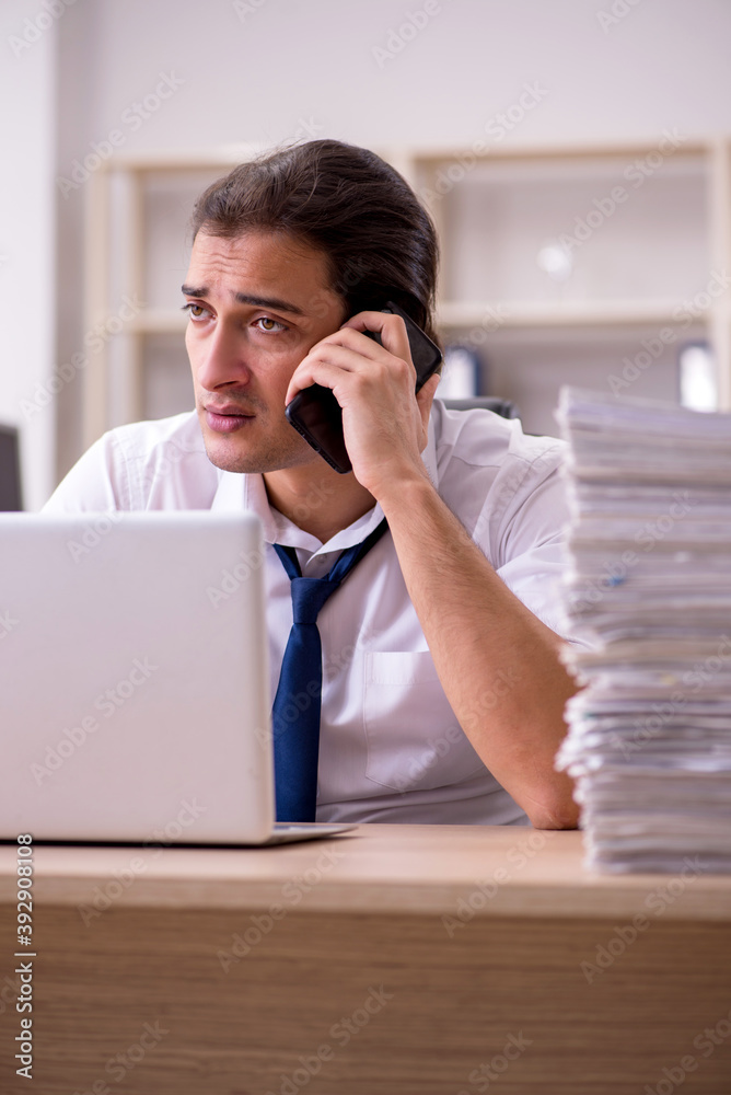 Young male employee unhappy with excessive work in the office Young male employee unhappy with excessive work in the office