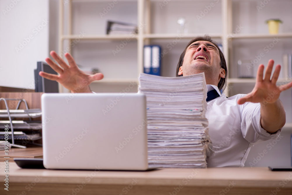 Young male employee unhappy with excessive work in the office Young male employee unhappy with excessive work in the office