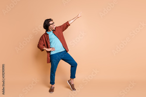 Full length profile photo of guy dance direct finger up wear spectacles brown t-shirt pants footwear isolated beige color background