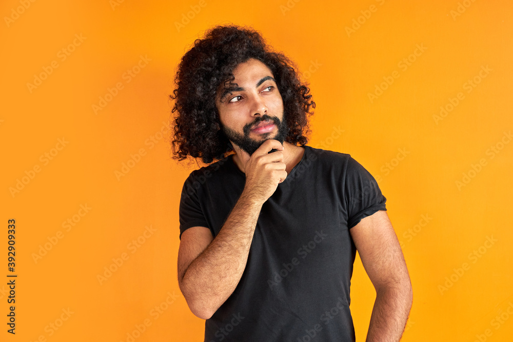 determined arabic male with beard is thinking and looking worried, standing against orange background. determined arabic male with beard is thinking and looking worried, standing against orange background.