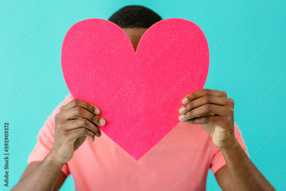 © Carlos David - Close up portrait of a young man holding pink heart in front of head with face obscured, valentineÕs day love, give your heart concept