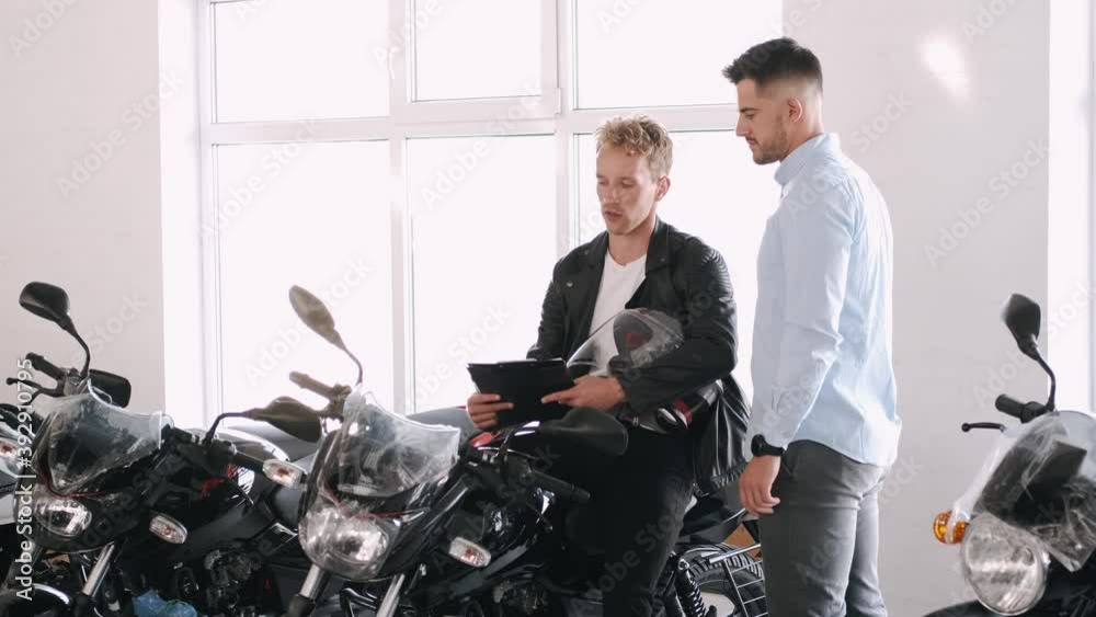 Handsome customer listening to motorcycle salon manager. The client is going to buy a motorbike. Dealership, sports shop. Biker lifestyle.