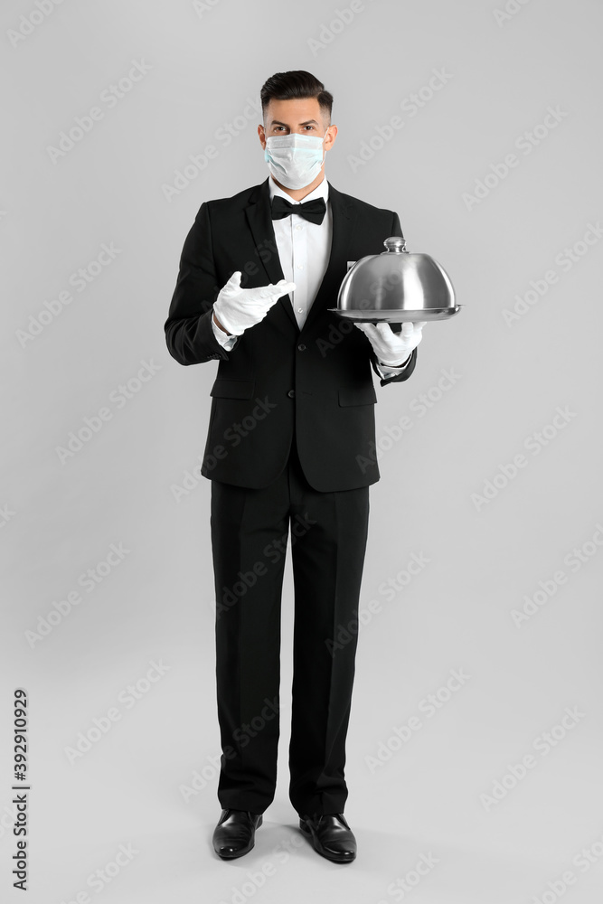 Waiter in medical face mask holding tray on light grey background Waiter in medical face mask holding tray on light grey background