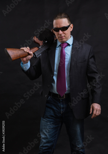 Mature gangster in sunglasses dressed in suit with tommy gun