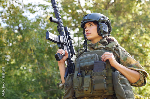 strong brave female army soldier with rifle machine gun standing in the forest, she is ready to shoot at enemy, firearm outdoor shooting range