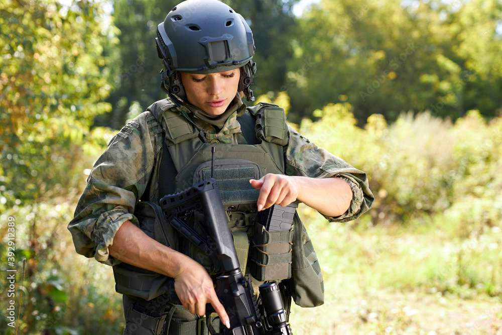 young caucasian military woman is checking rifle in the forest before shooting, alone in nature, female soldier