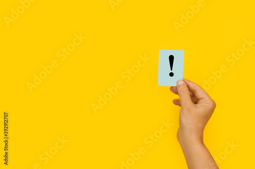 Mano de mujer sosteniendo un papel con el signo de exclamación sobre el fondo amarillo brillante liso y aislado. Vista de frente. Copy space  photo
