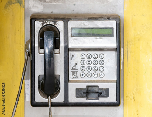 Shabby street telephone in booth, yellow background