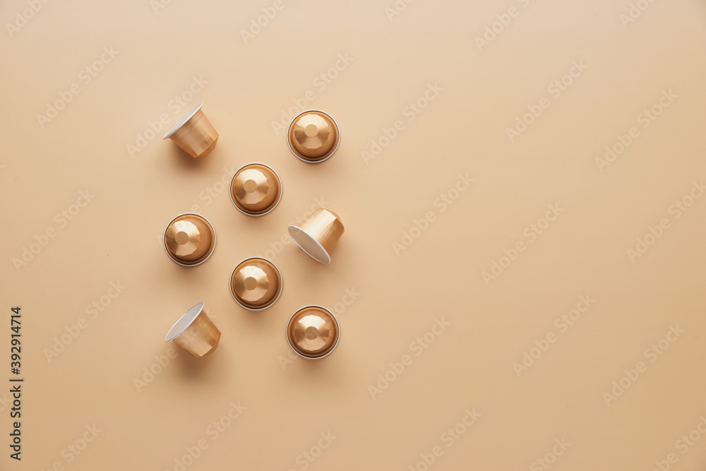 Caffeine, hot drinks and objects concept - close up of golden capsules or pods for coffee mashine on beige background. Top view with space for text. Flat lay..