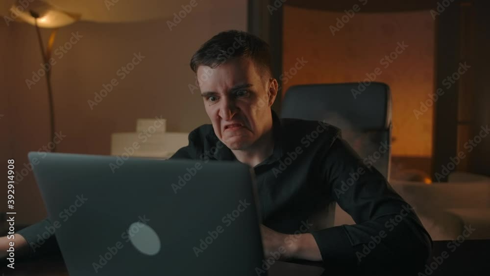 An angry hater starts to smoke Looking at the laptop screen. Anger and hate when browsing social networks and reactions to comments concept. An angry hater starts to smoke Looking at the laptop screen. Anger and hate when browsing social networks and reactions to comments concept.