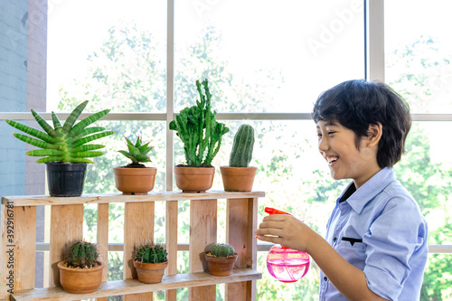 Young Asian boy smilimg, watering, enjoy beautiful and healthy cactus and succulent in glasshouse. Hobby can be starting point of learning and business. Plant caring and gardening concept.