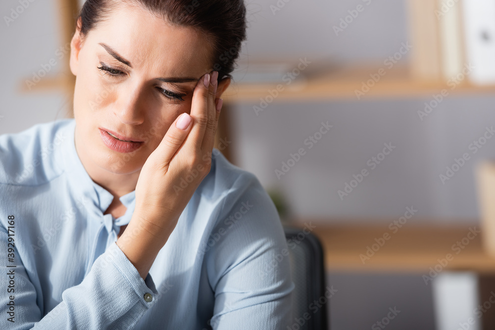 Portrait of brunette woman with migraine, holding hand near temple and looking away on blurred background Portrait of brunette woman with migraine, holding hand near temple and looking away on blurred background