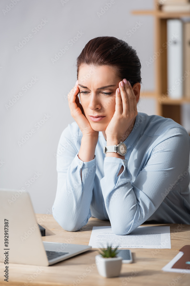 Tired brunette businesswoman with headache leaning on workplace on blurred background Tired brunette businesswoman with headache leaning on workplace on blurred background