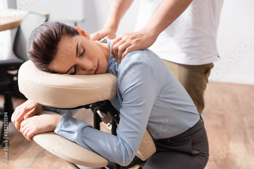 Schilderij op canvas Massage therapist massaging shoulders of woman with closed eyes, sitting on mass