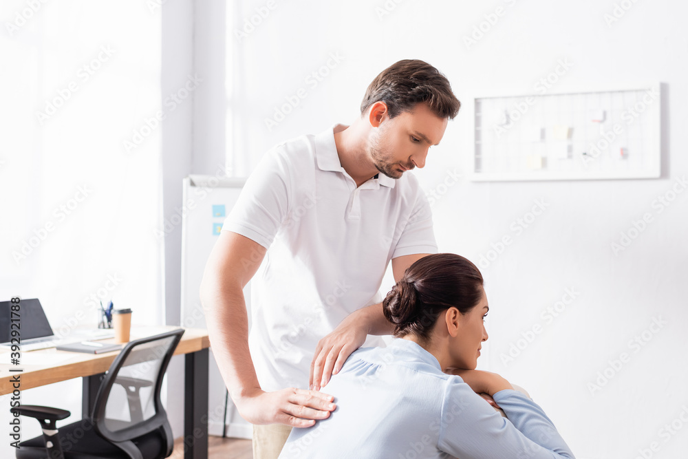 Obraz premium Focused masseur looking at brunette woman, while doing back massage in office