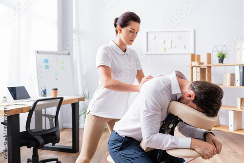 Masseuse doing seated massage of businessman back in office