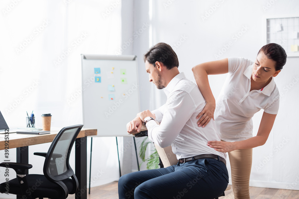 Masseuse doing seated massage of back for businessman in office Masseuse doing seated massage of back for businessman in office