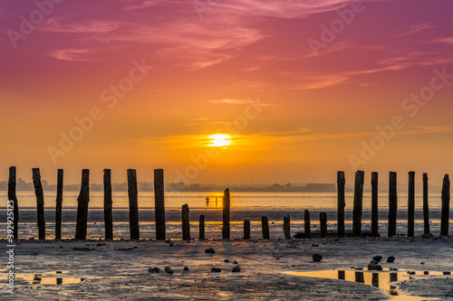 A stunning vibrant and colourful Sunset at West Wittering beach in West Sussex, England with reflections in puddles and old wooden posts with people playing in the background