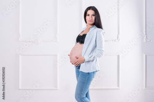 Happy pregnant girl in jeans and unbuttoned shirt
