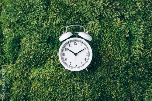 Alarm clock on green grass, moss background. Top view. Copy space. Ecology of sleeping