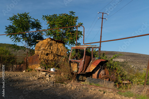 Old rusty and abandoned tractor on the street with some fodder in the background in the town of Azokh part of the Janapar Trail in Nagorno Karabakh in the Republic of Artsakh photo