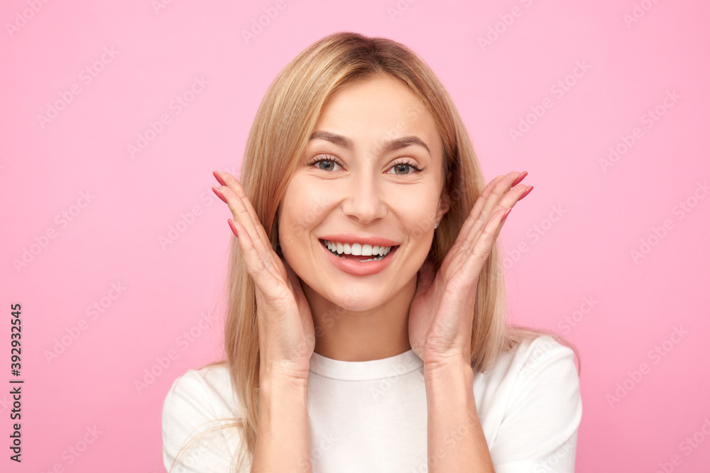 Blonde positive girl raises palms from joy and smiles in a casual white t-shirt, heard amazing news, happy to receive incredible surprise present isolated in pink studio Blonde positive girl raises palms from joy and smiles in a casual white t-shirt, heard amazing news, happy to receive incredible surprise present isolated in pink studio