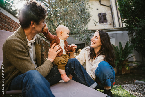 Young happy family having fun together in garden at home at lockdown - Mother and father playing with little baby son in a winter day at sun