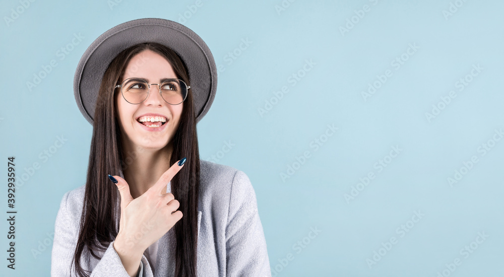 Image of happy young lady with gray hat standing isolated over blue background. Looking at corner and pointing. Image of happy young lady with gray hat standing isolated over blue background. Looking at corner and pointing.