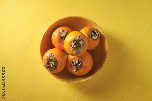 Orange persimmon on a yellow plate, on a yellow background, top view