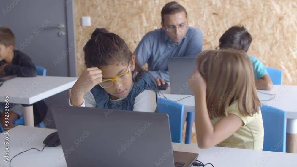 Computer science teacher sitting at desk near schoolboy. Pupils doing task or watching content in class. Digital education concept