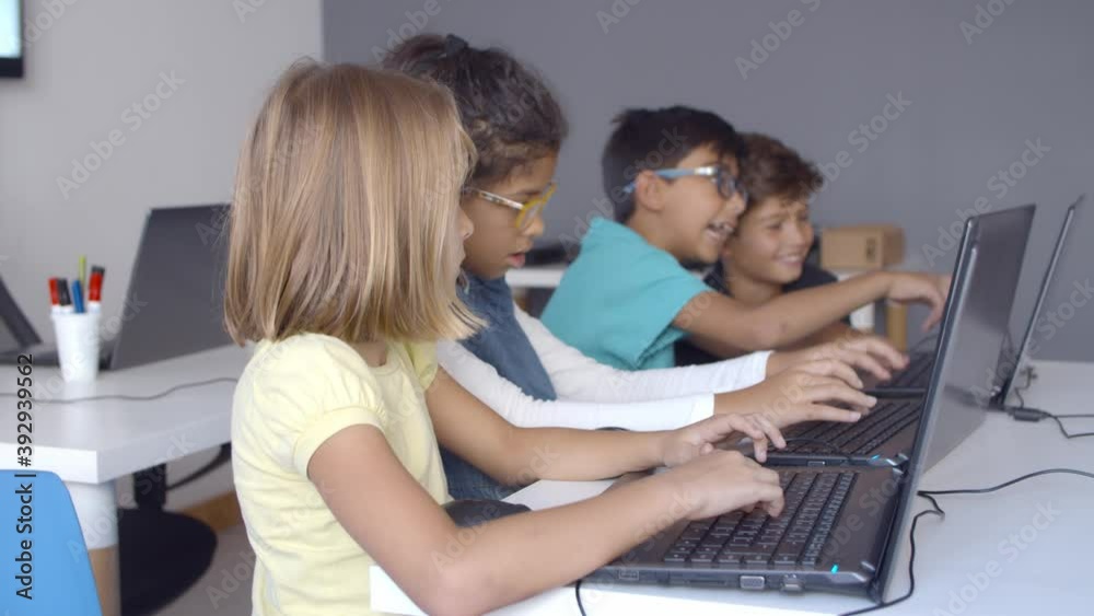 School pupils working on task together, using laptops, typing on keyboard, laughing during computer science class. Side view. Digital education and teamwork concept School pupils working on task together, using laptops, typing on keyboard, laughing during computer science class. Side view. Digital education and teamwork concept