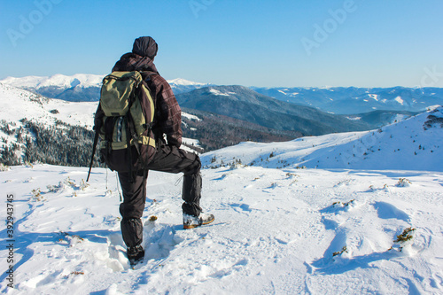 Man with backpack trekking in mountains. Cold weather, snow on Peaks. View back