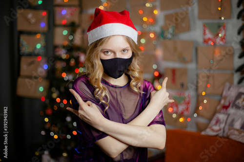 Portrait of a beautiful girl in medical mask, standing in front of decorated christmas tree at home