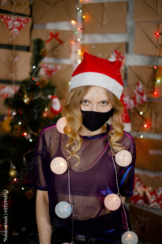 Portrait of a beautiful girl in medical mask, standing in front of decorated christmas tree at home