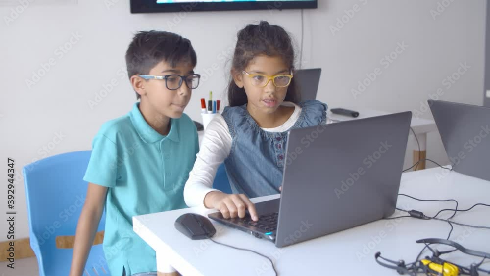 Two serious classmates in glasses working on task, using laptop in classroom. Static shot. Digital education concept