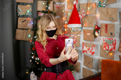 Portrait of a beautiful girl in medical mask, standing in front of decorated christmas tree at home