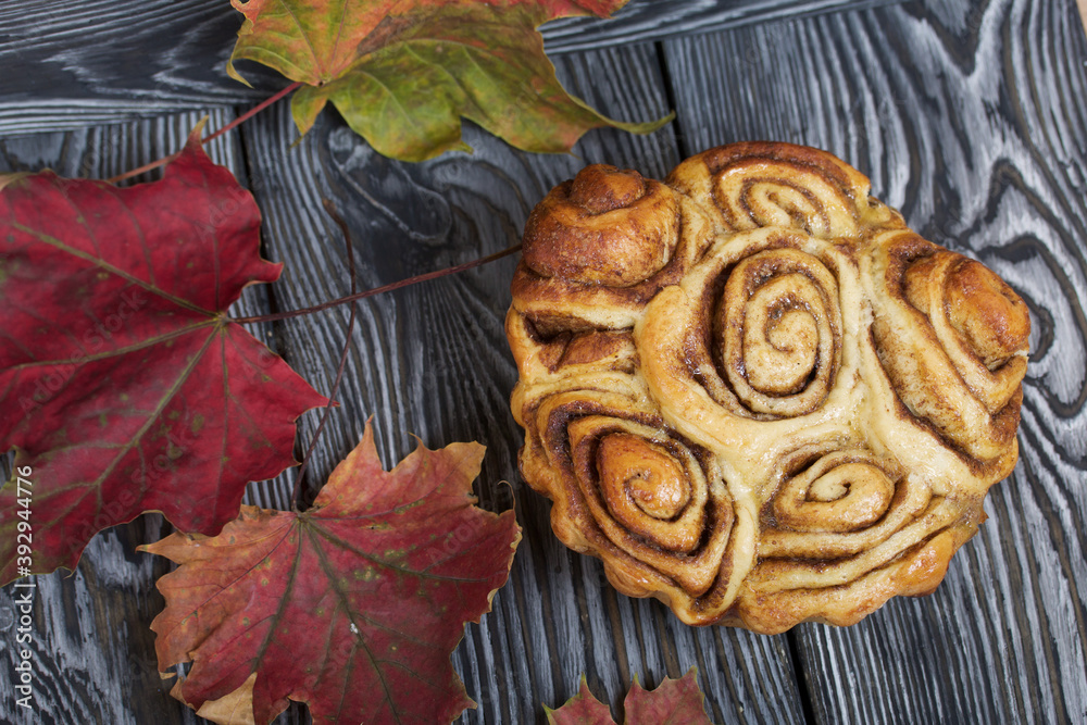 Baked cinnabons in shape. Stand on black composite boards. Nearby are autumn maple leaves.