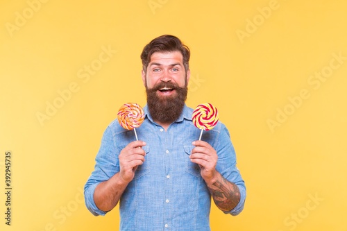 Happy bearded man hold tasty rainbow swirl candy pops great for birthday party and candy buffet yellow background, celebration