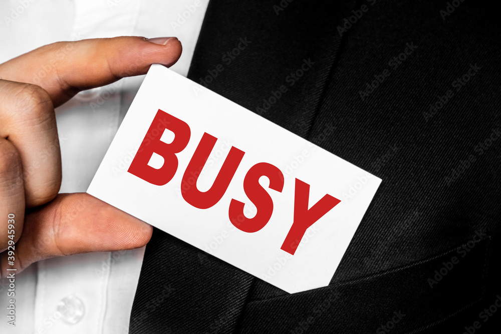 A man in a black business suit lowers or removes from his breast pocket a white business card with the inscription BUSY. Business concept