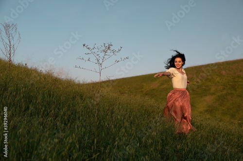 Smiling brunette woman dancing in fields during golden hour photo